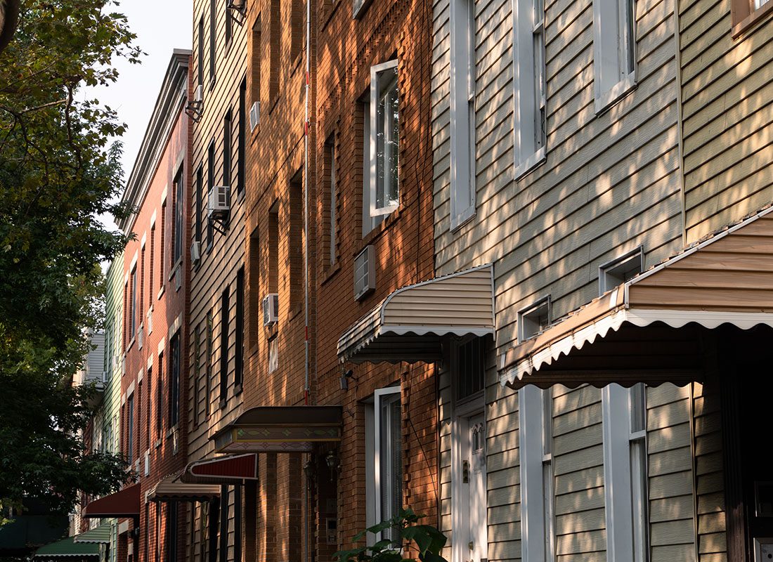 Contact - Row of Older Multi-Story Town Homes on a Sunny Day in Jamaica New York Shaded by Tall Green Trees in the Front